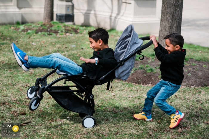 A Chicago documentary family photographer captured this stroller hijinks session with brothers outdoors on the grass A Chicago documentary family photographer captured this stroller hijinks session with brothers outdoors on the grass