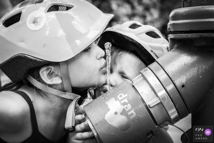 Nimes, Gard documentary family photography showing girls drinking water wearing helmets at a fountain in the public park