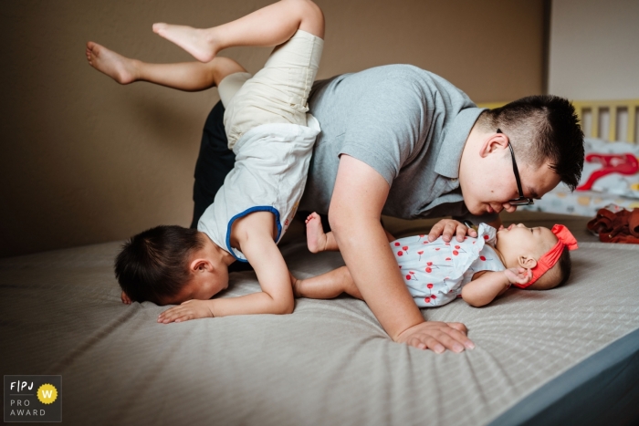 San Jose, California family photography of a super hero doing a scorpion move on the bed over dad and little sister