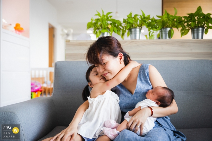 Ein Familienfotograf aus Singapur hat diese dicke Umarmung von der großen Schwester zu ihrer Mutter zu Hause festgehalten