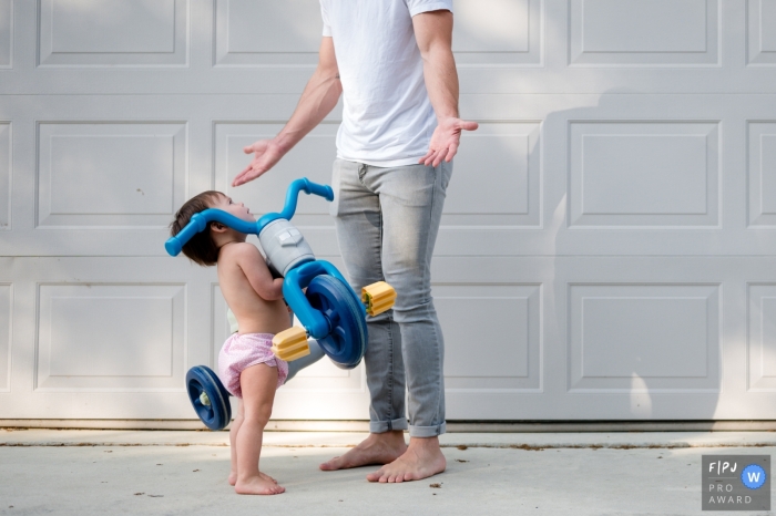 A Sarasota documentary family photographer from Florida captured this image as the Toddler asks her dad for up while holding up her toy tricycle A Sarasota documentary family photographer from Florida captured this image as the Toddler asks her dad for up while holding up her toy tricycle
