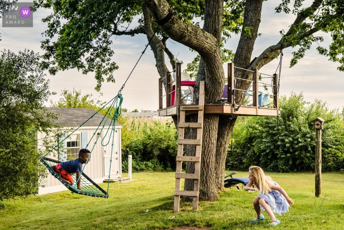 Awarded documentary family photo from New Hampshire of a little boy swinging in backyard while little girl laughs and pushes him Awarded documentary family photo from New Hampshire of a little boy swinging in backyard while little girl laughs and pushes him