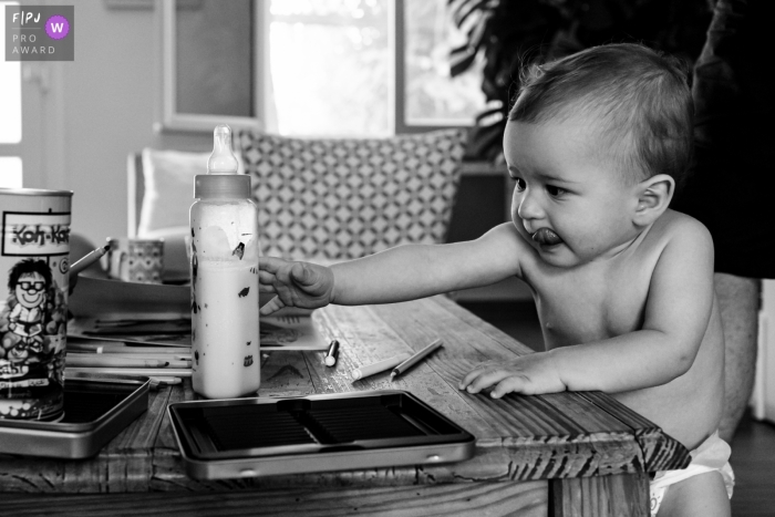 Awarded documentary family photo from Paris of baby grabbing the bottle with tongue out Awarded documentary family photo from Paris of baby grabbing the bottle with tongue out
