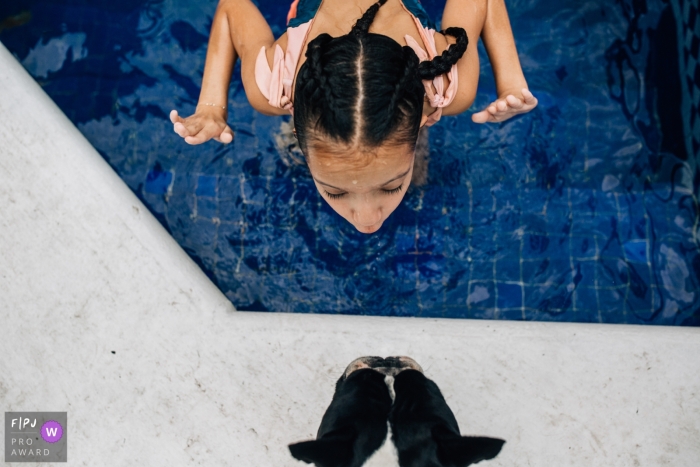 Preisgekröntes dokumentarisches Familienbild aus Mexiko-Stadt von einem Mädchen in einem Pool, das mit ihrem Hund auf dem Deck spielt