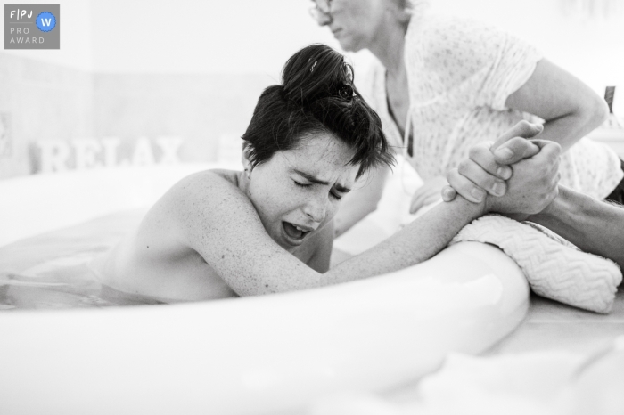 Mom endures one of the final contractions before meeting her baby in the birth tub in this Black and white Sarasota documentary birth picture from the Birthways Family Birth Center