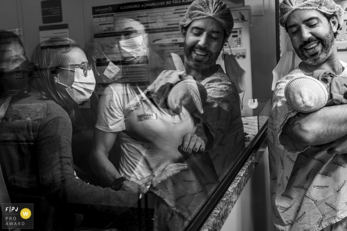 Black and white Belo Horizonte documentary birth picture from Mater Dei captured this father proudly showing off his newborn daughter to his family