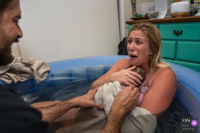 Ventura, CA, thuisbevaldocumentaire fotografie van moeder die haar man ongelovig aankijkt terwijl ze hun pasgeboren baby knuffelt