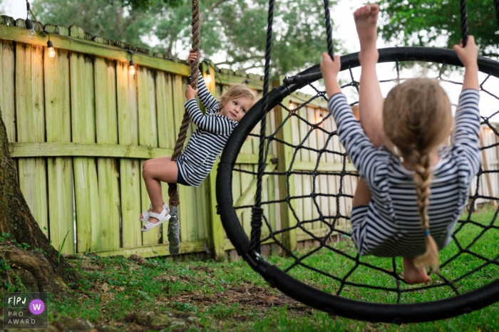 Sarasota meilleure photo de famille documentaire d'une session à domicile en Floride montrant des sœurs jouant sur la corde et des balançoires dans leur jardin après le dîner