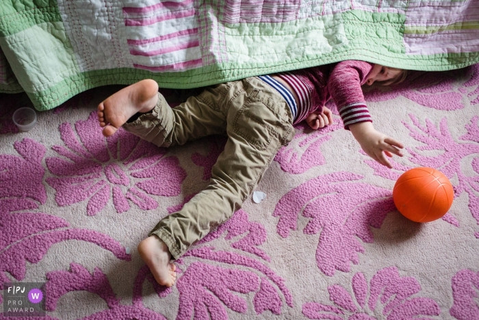 A young boy pushes his ball out from under the bed during a documentary family photojournalism session in New Hampshire A young boy pushes his ball out from under the bed during a documentary family photojournalism session in New Hampshire