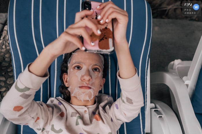 Documentary family photojournalism from Mexico City showing a teen on a lounge chair wearing a facial mask and holding a phone Documentary family photojournalism from Mexico City showing a teen on a lounge chair wearing a facial mask and holding a phone