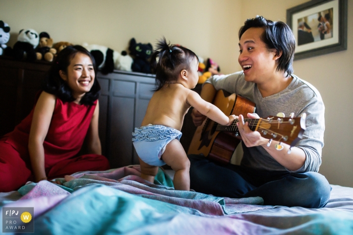 San Francisco best documentary family pictures from a home session with the baby appearing to suggest: Daddy I can play the guitar too?