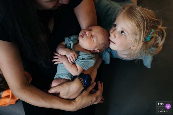 A Madison Mother holds newborn while sister looks up at mother during a Wisconsin home session A Madison Mother holds newborn while sister looks up at mother during a Wisconsin home session