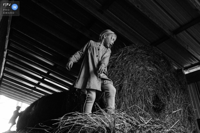 A Madison Wisconsin young girl stands on a large hay bale with a silhouette of her younger sister in the background