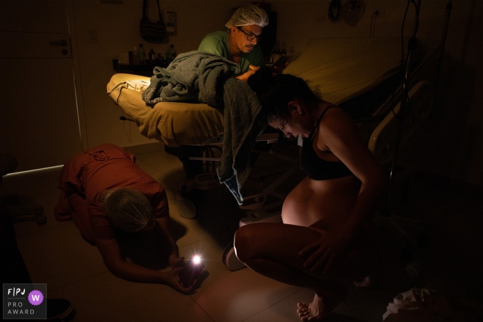 At Santa Clara hospital, a father anxiously awaits the birth of his child while a nurse monitors the mother in labor At Santa Clara hospital, a nurse watches a mother in labor while the father checks his cell phone