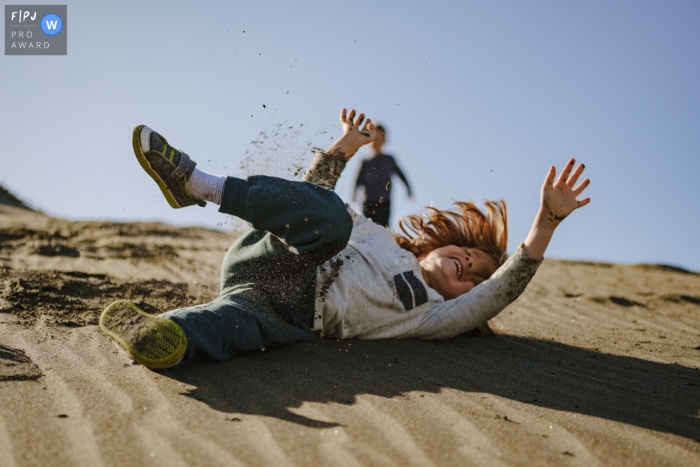 In San Francisco, California, two brothers enjoy an afternoon of sand dune rolling A young boy rolls down a sandy dune in San Francisco, California, as his brother observes from the top