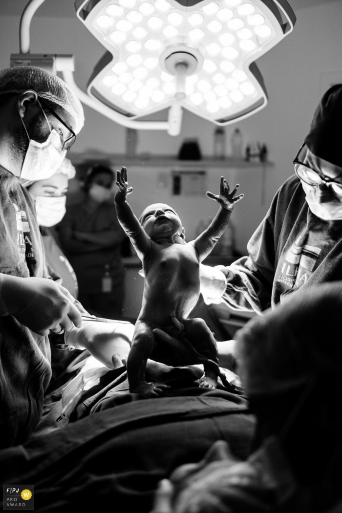 Pasgeboren baby die zijn armen opent op het moment van geboorte, met tegenlicht, vastgelegd tijdens een geboortefotosessie in Hospital Ilha Maternity