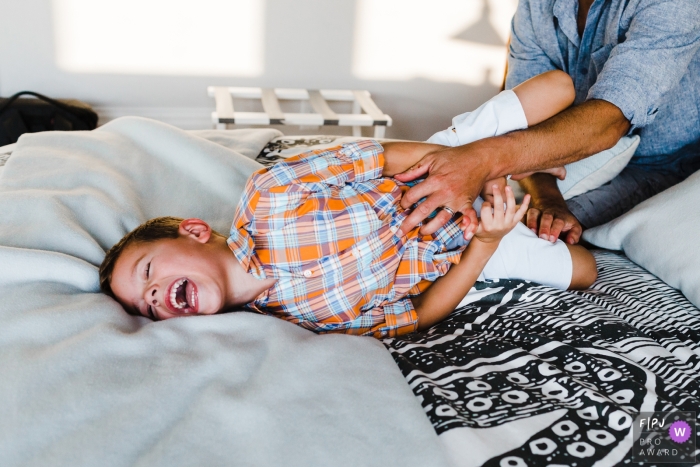 In New Hampshire, a photographer captured an adorable family moment, showcasing a young boy's uncontrollable laughter as his dad tickles him on the bed A photographer in New Hampshire beautifully captured a precious family moment, with a young boy laughing uncontrollably as his dad playfully tickles him on the bed