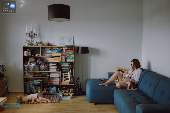 In Tallinn, Harju County, a photographer captures a heartwarming moment as a second child takes a peaceful nap by the bookshelf while the mother tends to another child