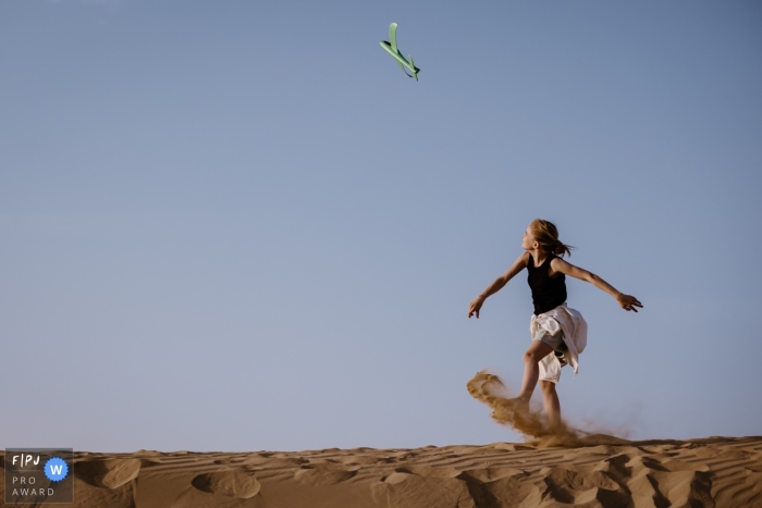 Dunes and Dreams: A Captivating Glimpse of Playtime in Dubai In Dubai, United Arab Emirates, a photographer captures a documentary picture of a young girl enjoying playtime with a toy flying plane on the sand dunes under a beautiful blue sky