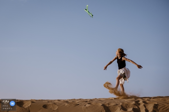 In Dubai, Verenigde Arabische Emiraten, maakt een fotograaf een documentair beeld van een jong meisje dat geniet van speeltijd met een speelgoedvliegtuigje op de zandduinen onder een prachtige blauwe lucht